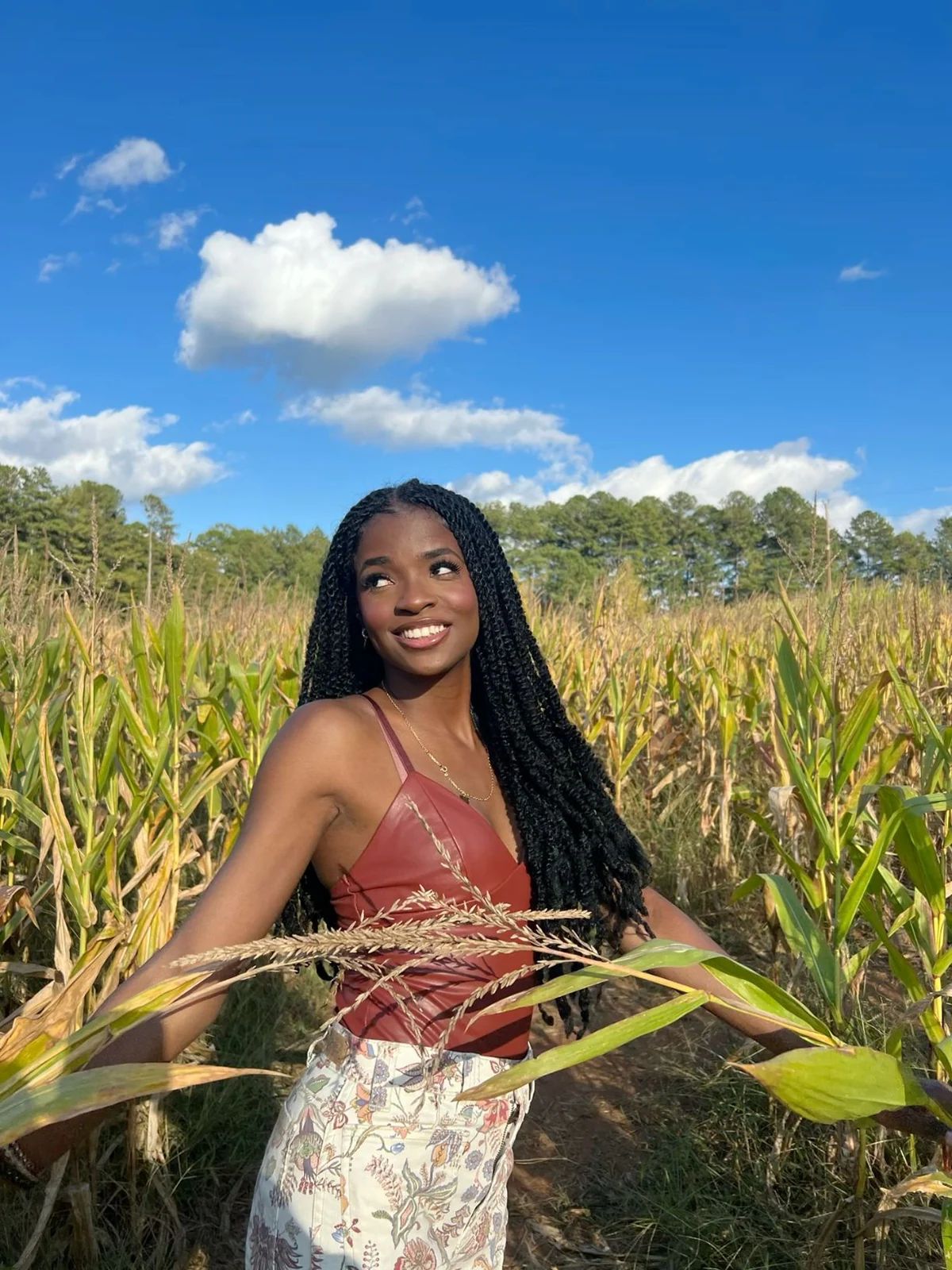Woman in rust leather top and floral maxi skirt standing in a cornfield at a fall farm