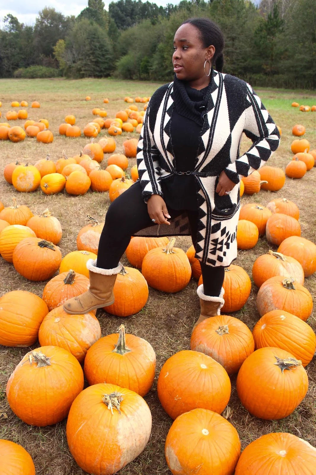Woman in black and white geometric knit cardigan with tan shearling boots standing in a pumpkin field
