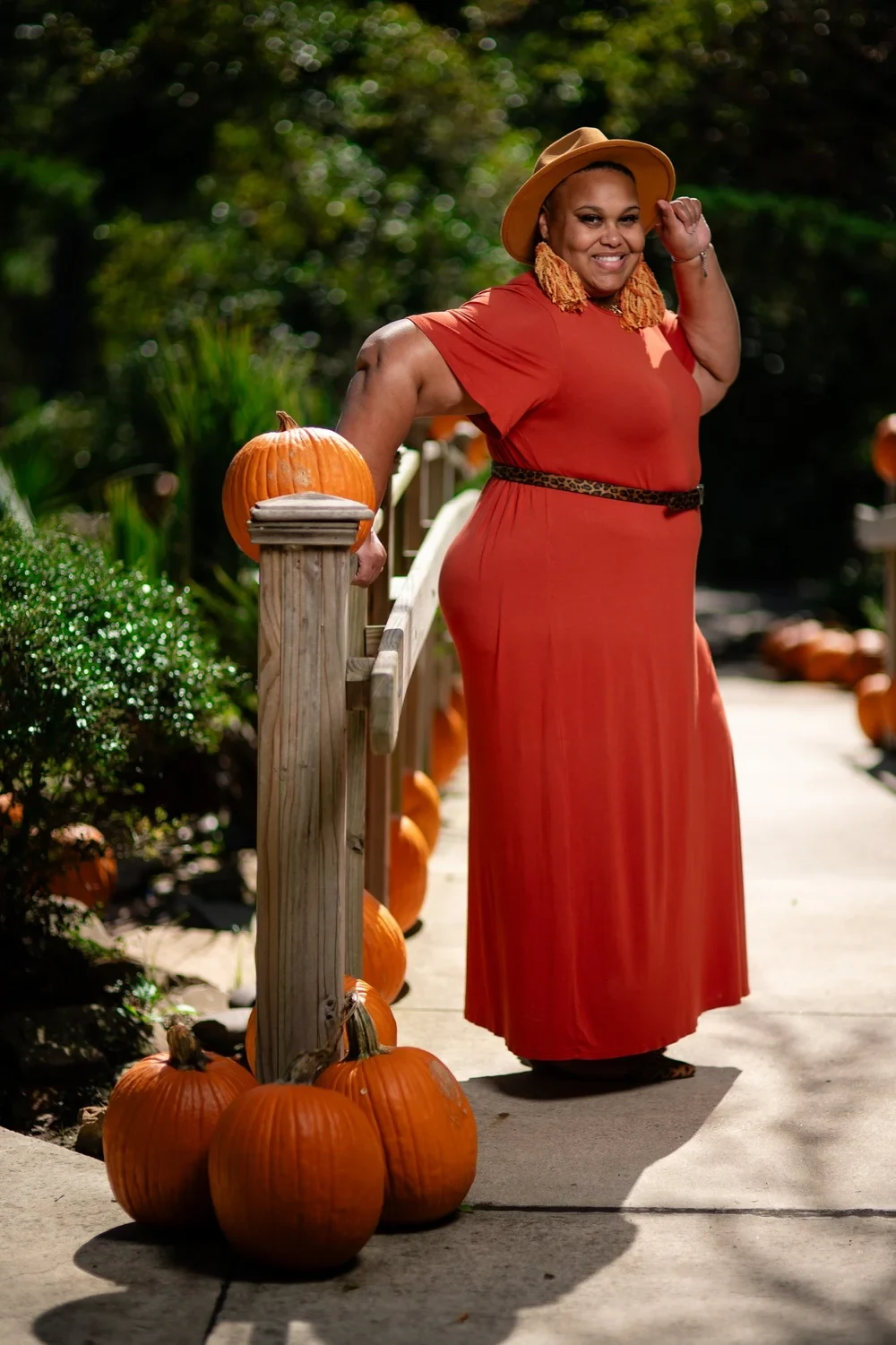 Woman in burnt orange maxi dress with leopard print belt and tan hat among pumpkins