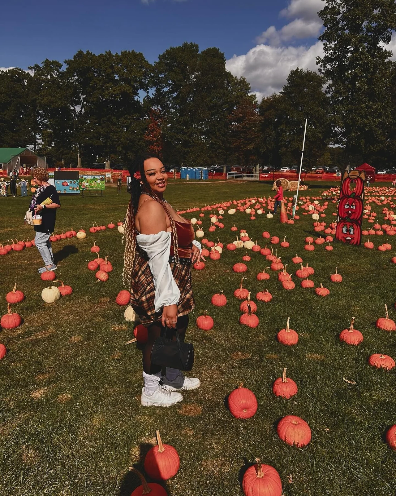 Woman in rust and white off shoulder top with plaid skirt and sneakers at a pumpkin festival