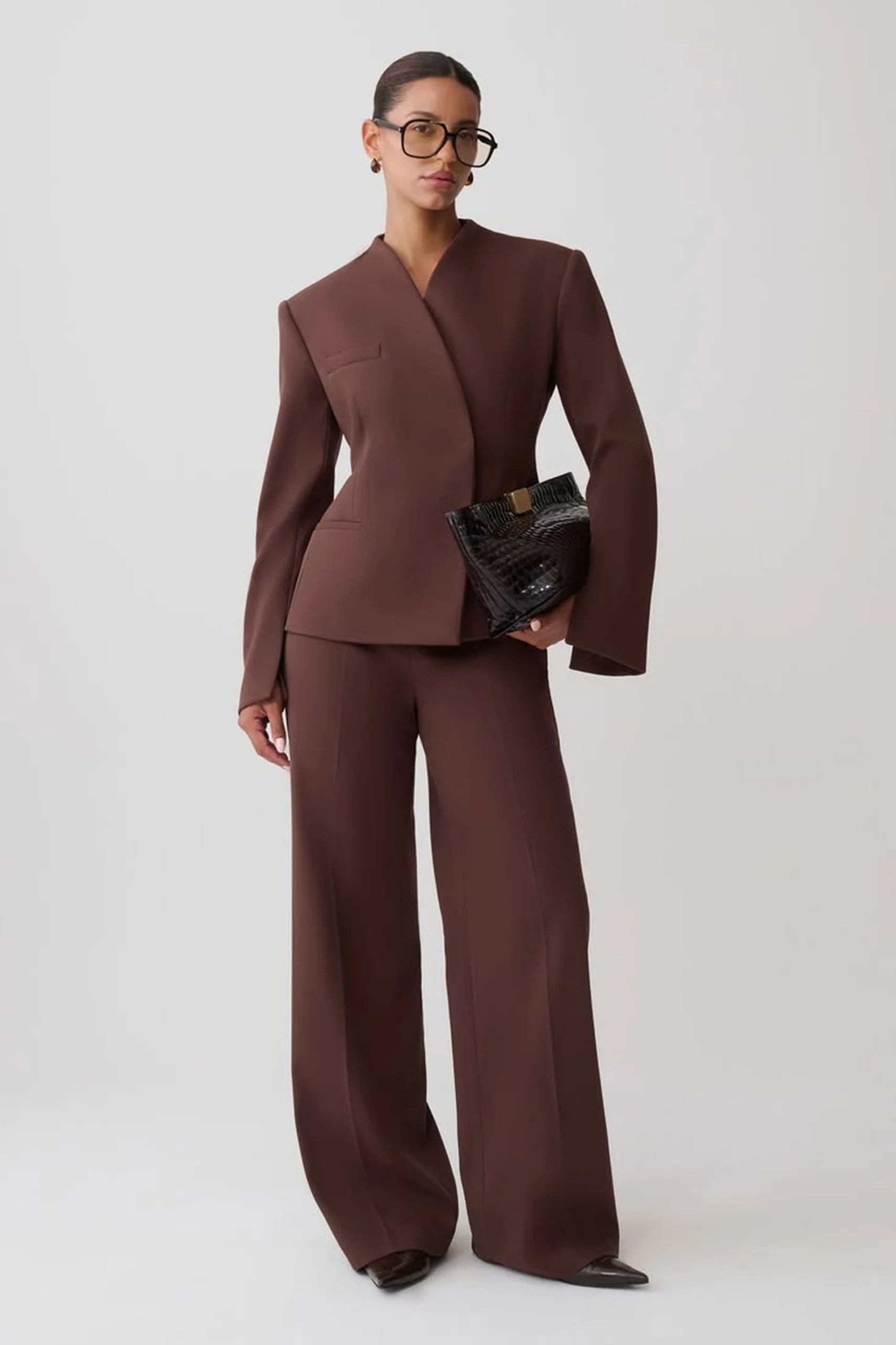 Woman in a tailored chocolate brown suit with wide leg trousers holding a black clutch