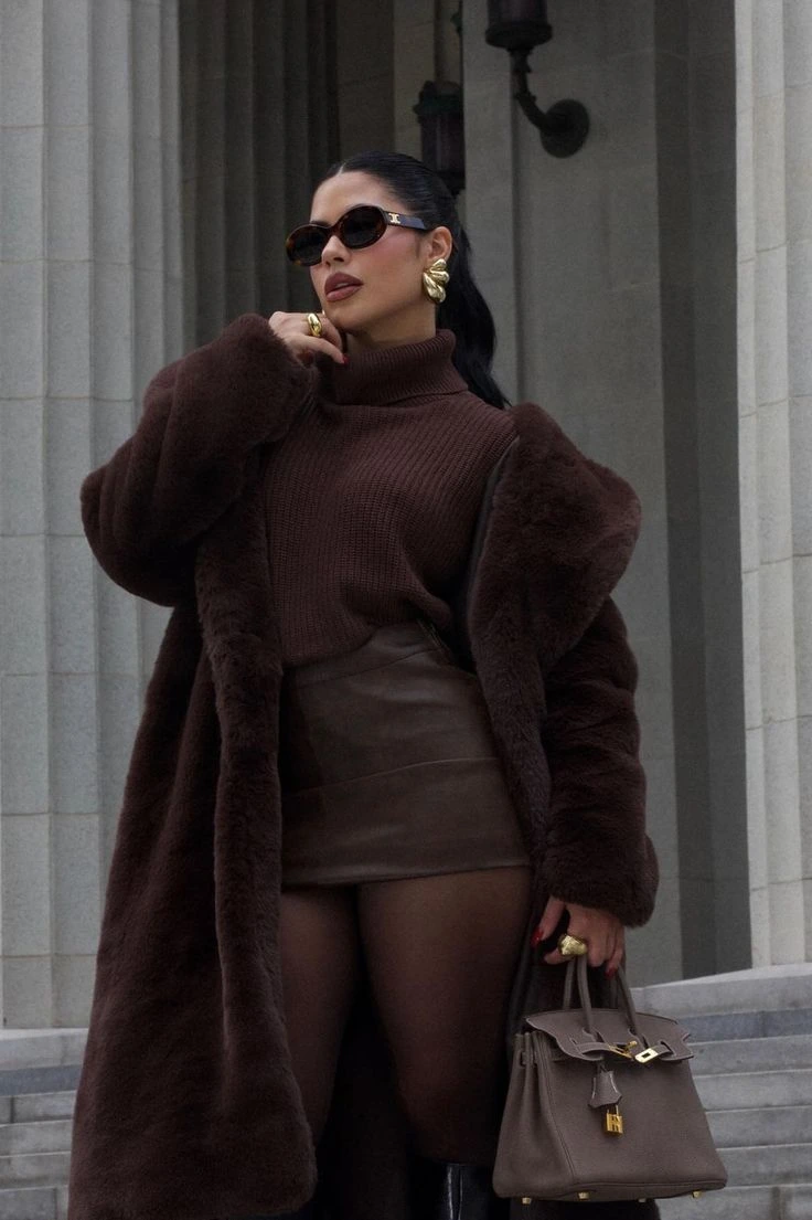 Woman in a chocolate brown faux fur coat over a knit top and leather mini skirt