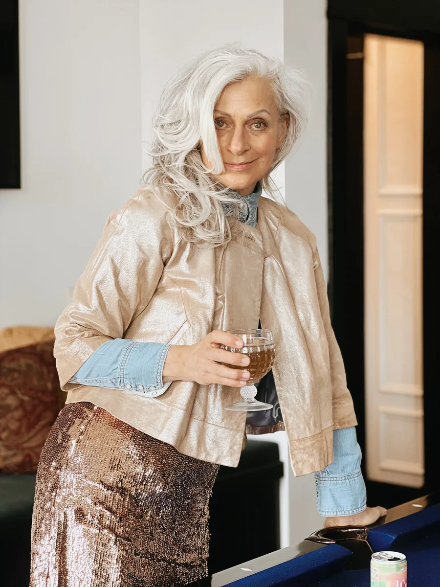 Mature woman in champagne jacket and sequin skirt with drink