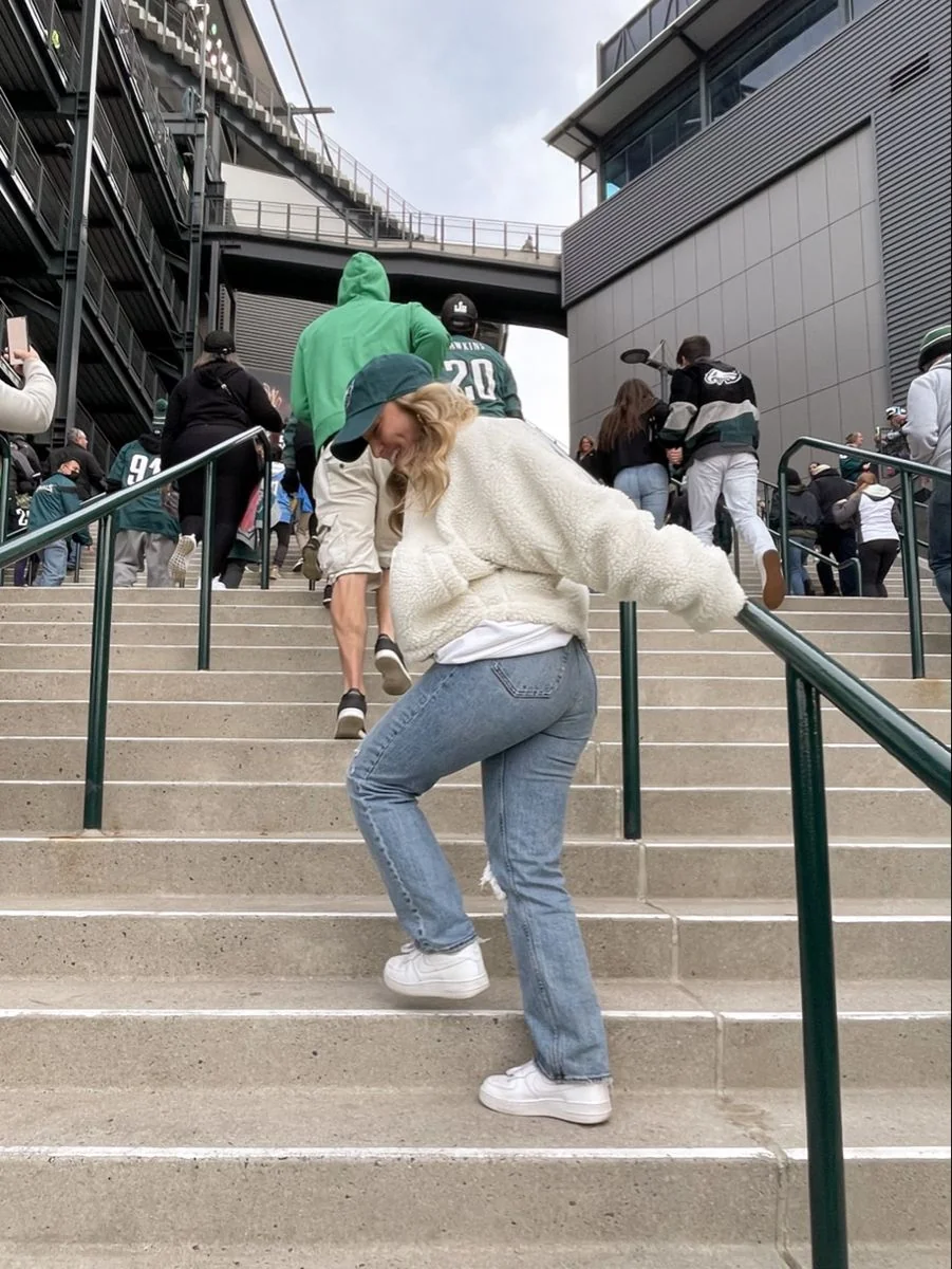 Woman in a cream top and jeans at a football stadium