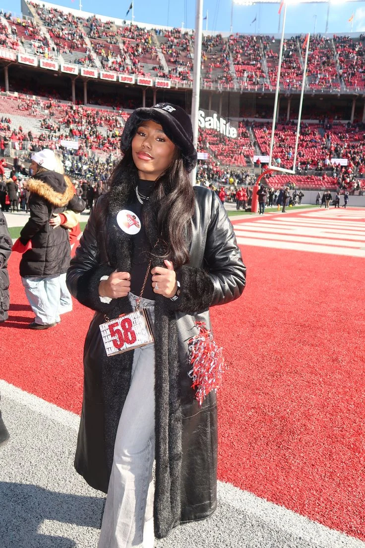 Fall game day outfit for Black women: long black faux fur-trimmed leather coat with light jeans at the stadium