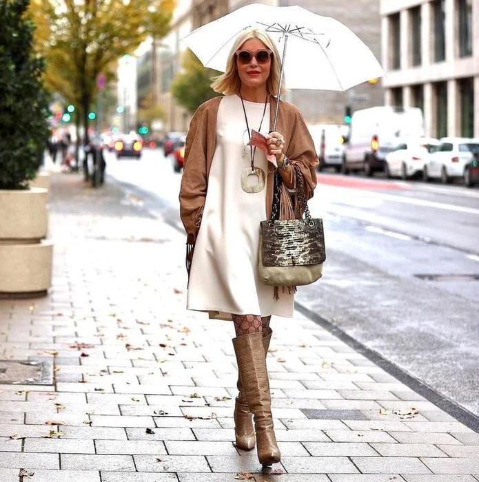 Fall rainy day outfit: cream coat and tall brown boots under a white umbrella
