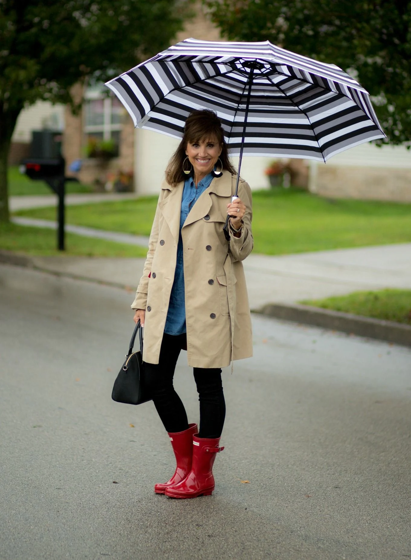 Fall rainy day outfit: beige trench with a striped umbrella and red boots