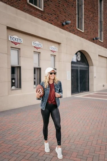 Plus size fall game day outfit: denim jacket with plaid scarf holding a football
