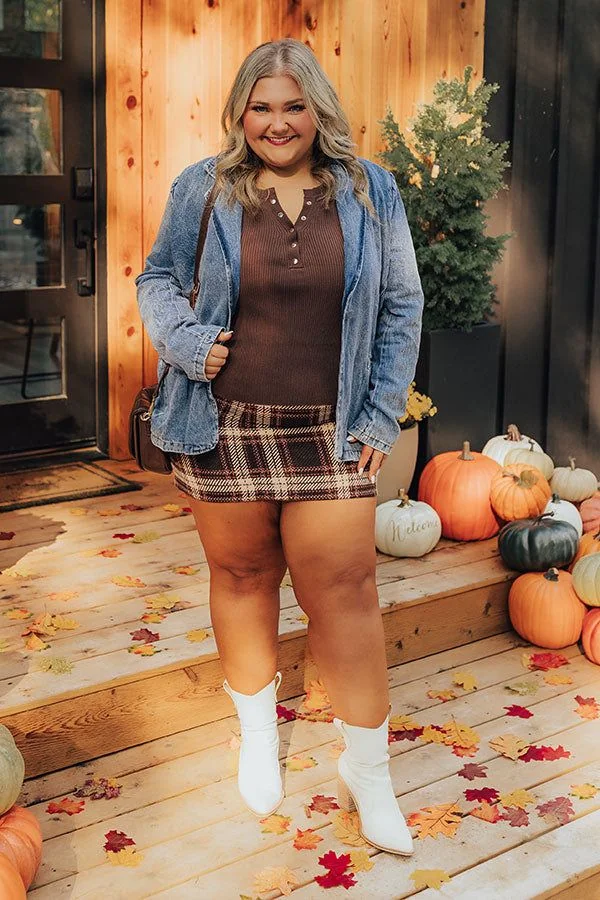 Plus size fall game day outfit: denim jacket over brown top with plaid mini skirt and white boots