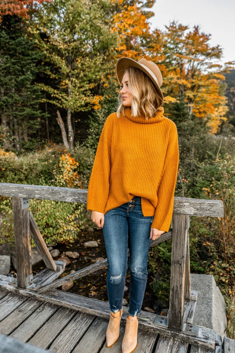 Plus size fall game day outfit: mustard knit sweater with medium wash jeans and ankle boots