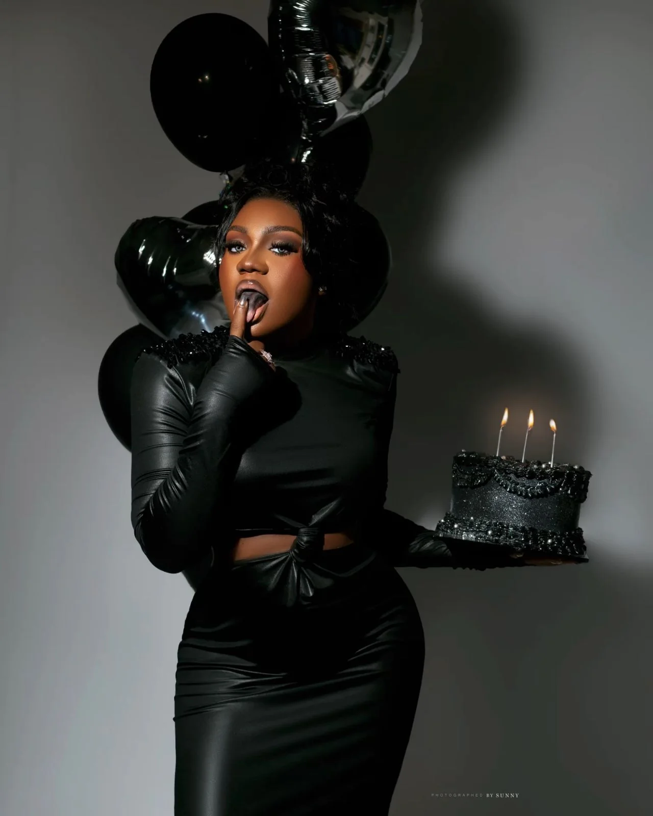 Black mini dress holding a birthday cake with black balloons