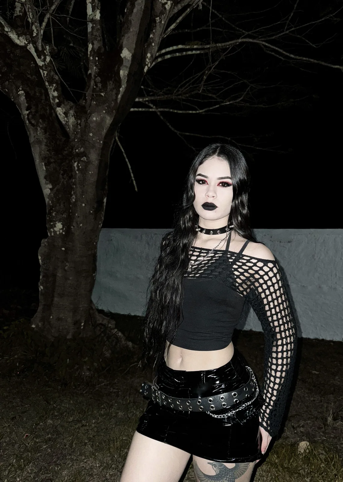 III points festival outfit: black fishnet-sleeve top with buckled mini skirt at night