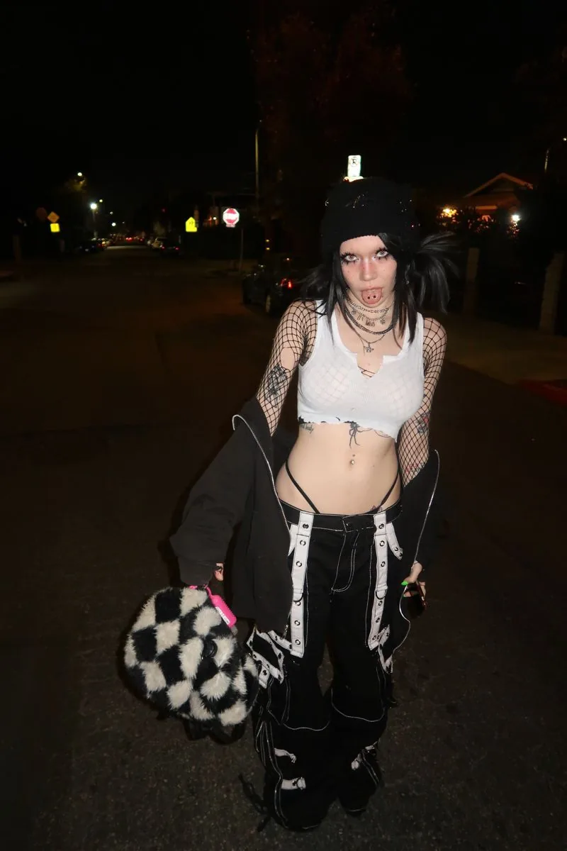 III points festival outfit: white fishnet crop top with baggy black pants on a dark street