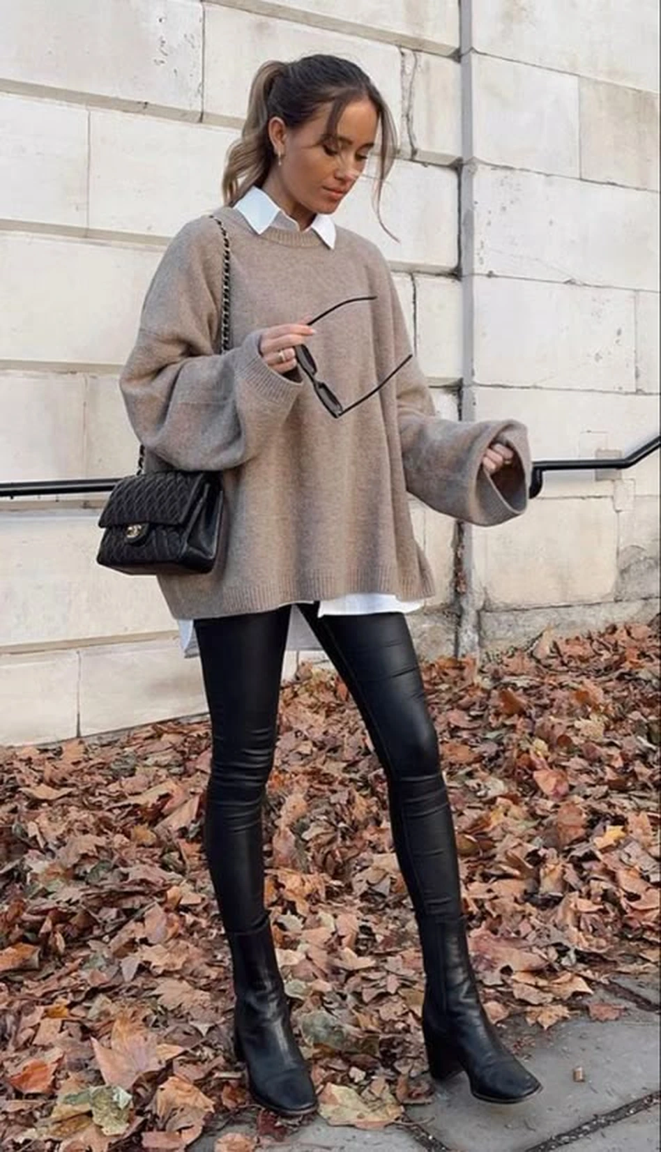 Woman wearing a slouchy taupe sweater over a white shirt with black leather leggings and heeled boots