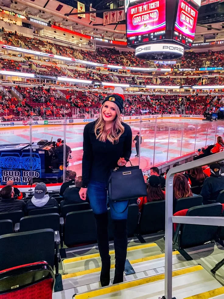 Woman in a black top, denim skirt, beanie and boots on arena stairs