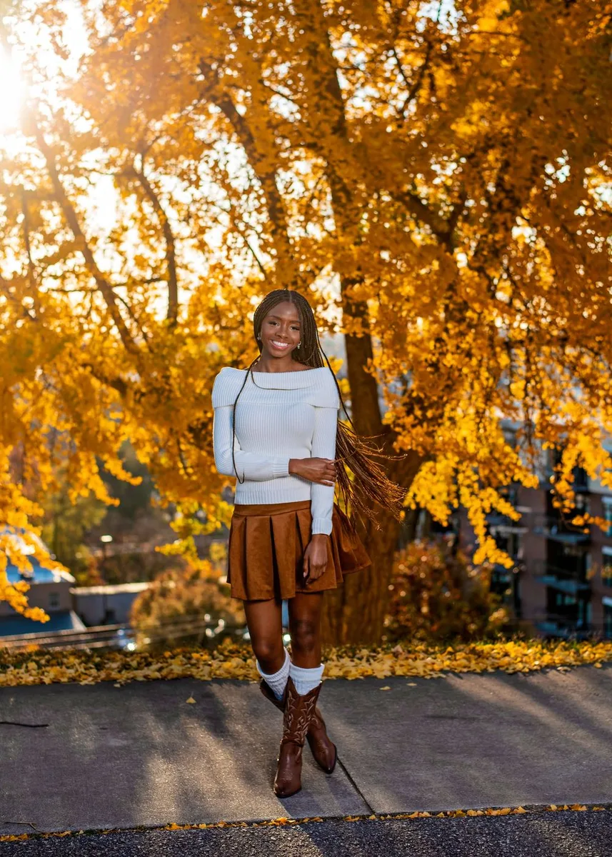 Black woman in a white top and brown skirt under autumn trees on campus