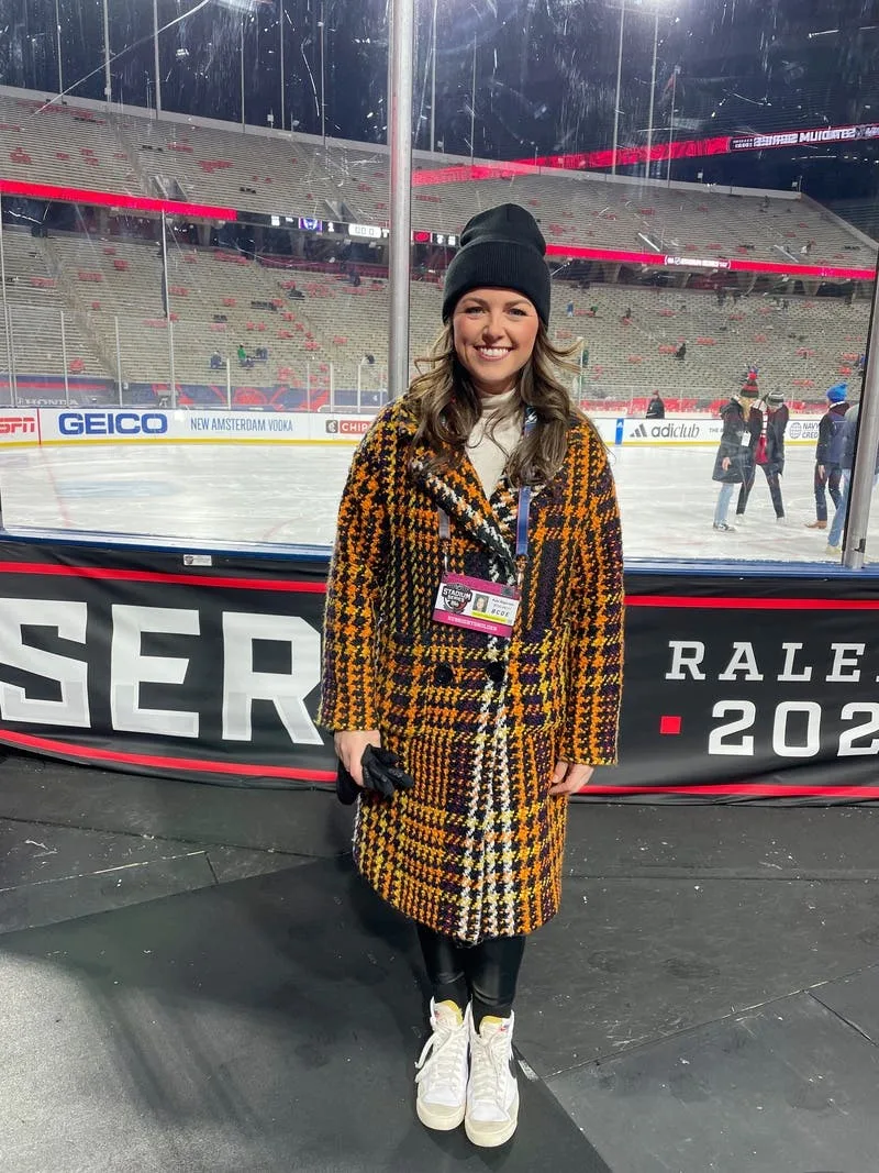 Woman in a plaid coat, beanie and white boots by the rink