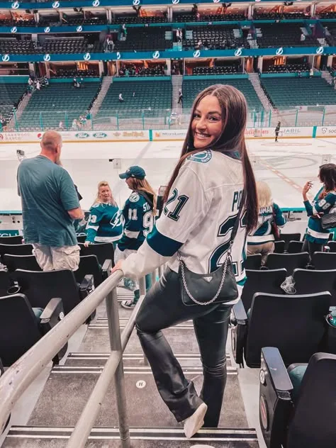 Woman in a white hockey jersey and jeans on arena stairs