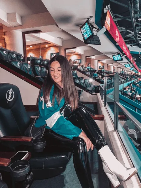 Woman in a teal hockey jersey, leather pants and white boots in a luxury box