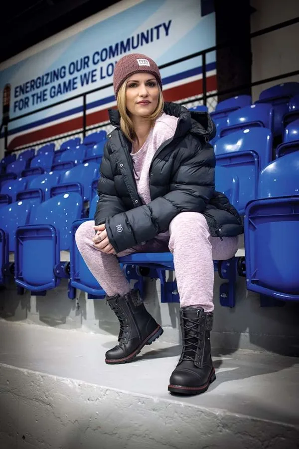 Woman in a black puffer jacket, beanie and boots in blue arena seats