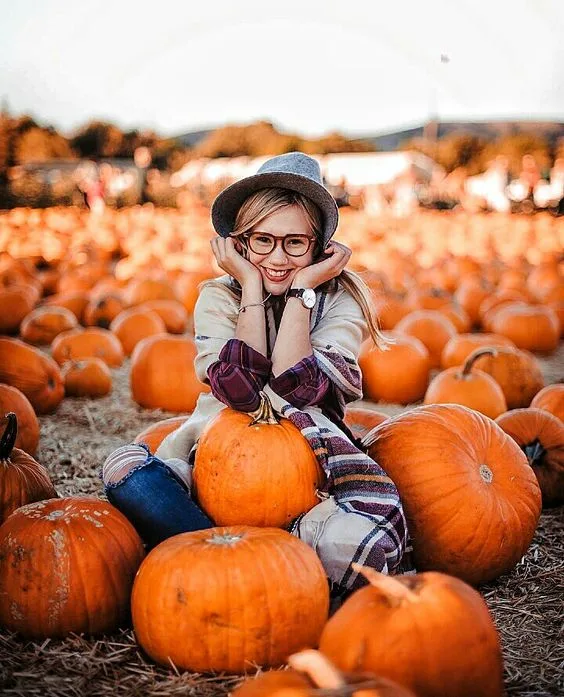 Pumpkin patch outfit: plaid shirt and jeans with a felt hat sitting among pumpkins
