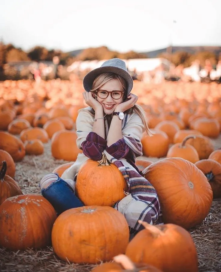 Pumpkin patch outfit idea: plaid shirt with a wide brim hat sitting between pumpkins