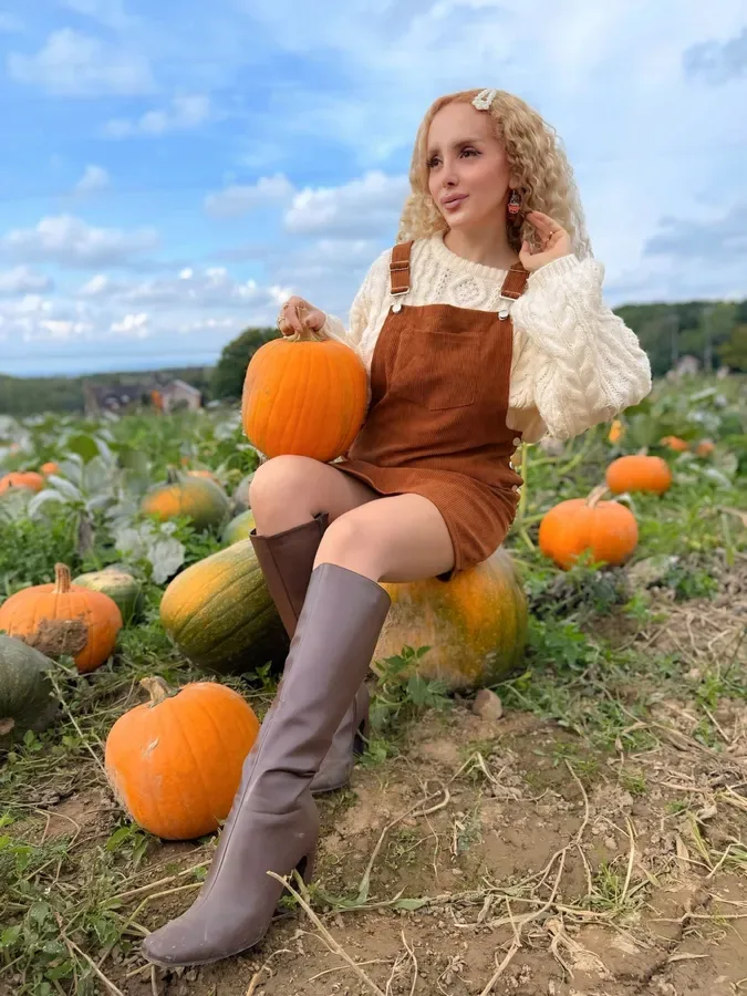 Fall pumpkin patch outfit: rust knit sweater with tall boots sitting on a hay bale