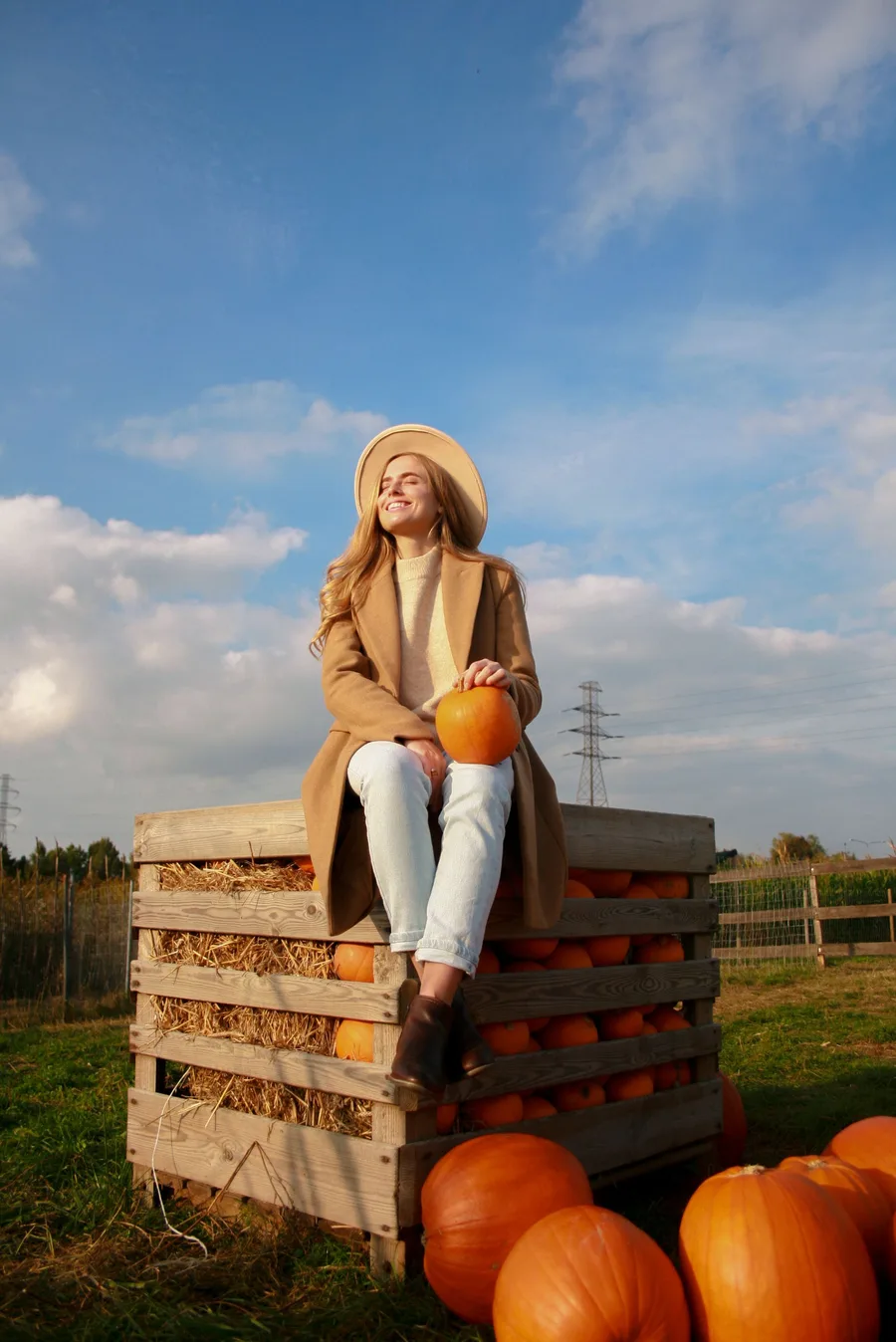 Pumpkin patch photo outfit: tan coat with white jeans sitting on wooden crates
