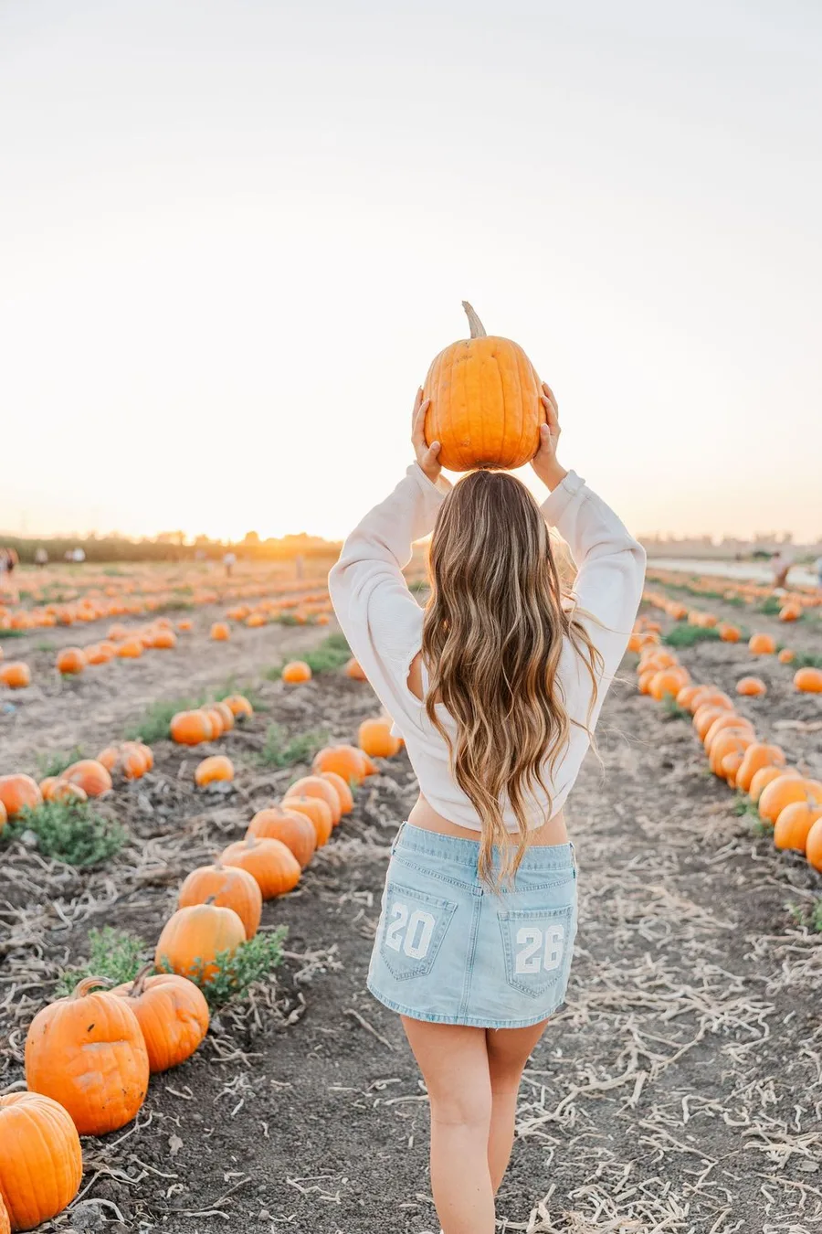 Hot weather pumpkin patch outfit: white top with denim shorts holding a pumpkin overhead