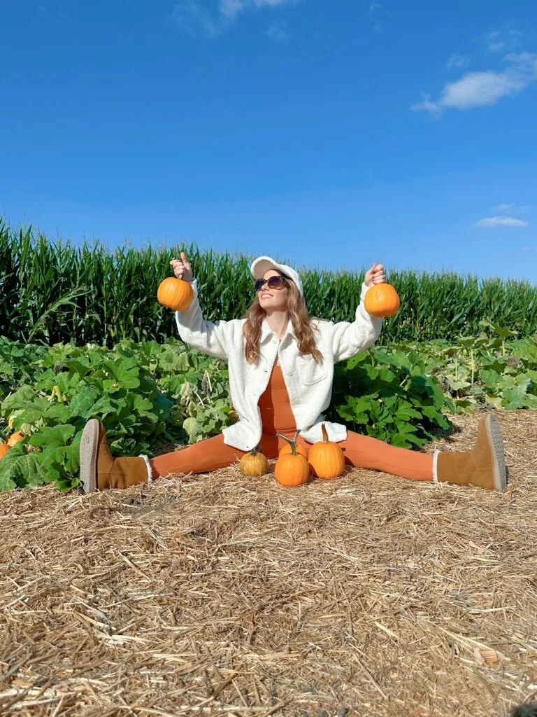 Playful pumpkin patch outfit: white shirt with an orange top sitting among pumpkins