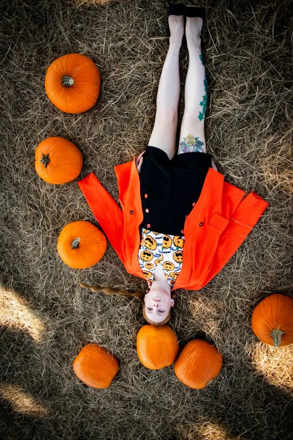 Artistic pumpkin patch outfit: bright orange coat lying among pumpkins from above