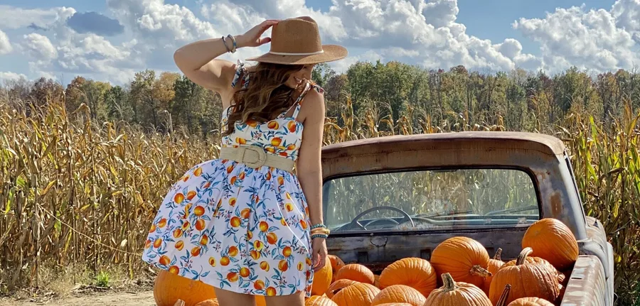 Cute pumpkin patch outfit: blue floral mini dress with a straw hat by the truck