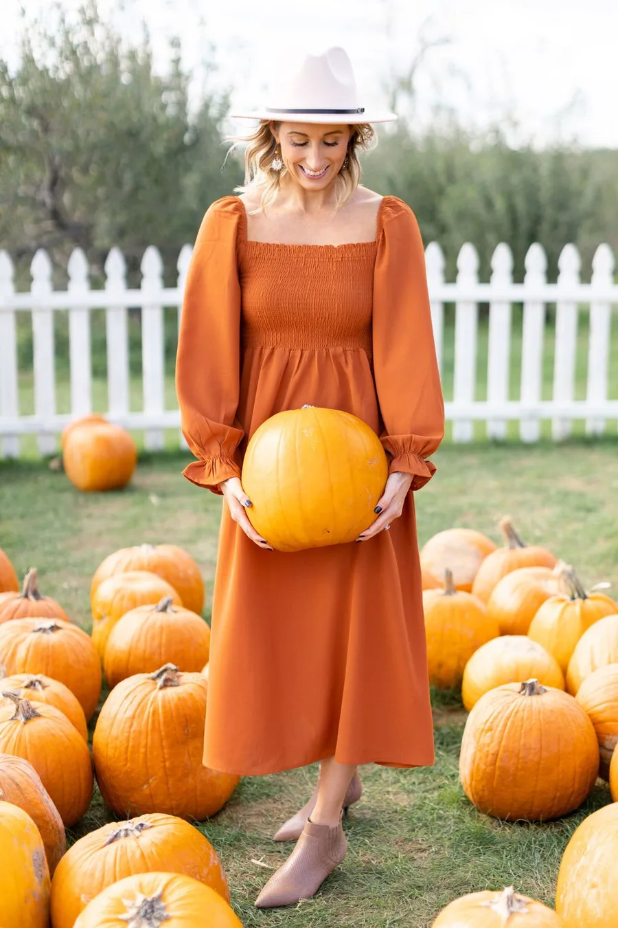 Pumpkin patch outfit: burnt orange midi dress with a white sun hat holding a pumpkin
