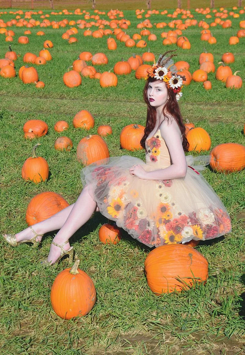 Pumpkin patch outfit idea: yellow floral mini dress sitting among pumpkins