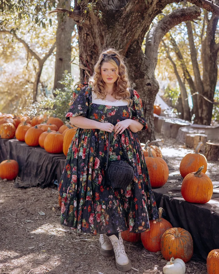 Pumpkin patch outfit: dark floral midi dress with white boots among pumpkins