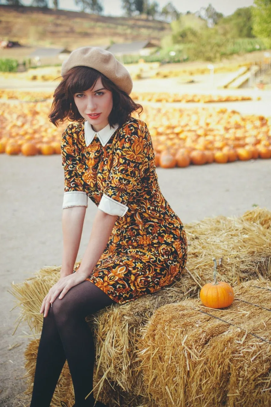Pumpkin patch outfit: orange floral dress with a straw hat sitting on hay bales