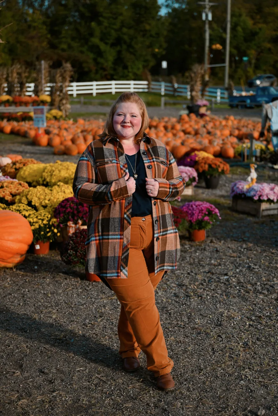 Plus size pumpkin patch outfit: plaid shirt with rust pants standing in the field