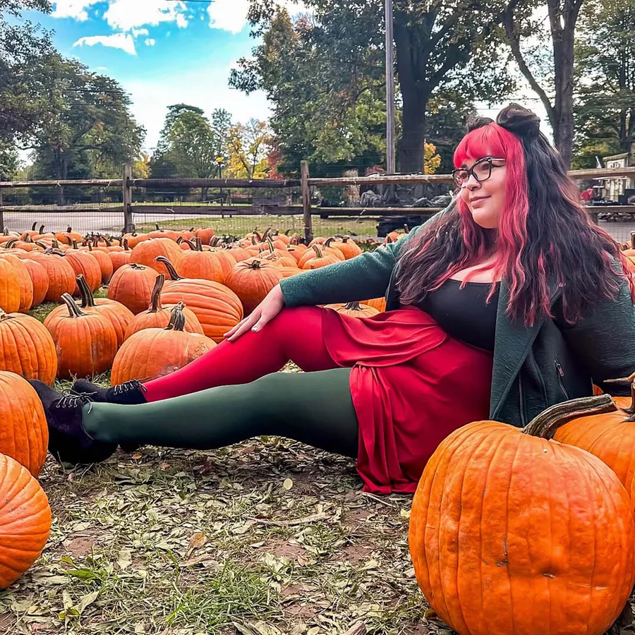 Plus size pumpkin patch outfit: red skirt with green tights sitting among pumpkins