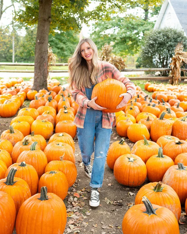 Pumpkin picking outfit: pink plaid shirt with jeans walking with a pumpkin