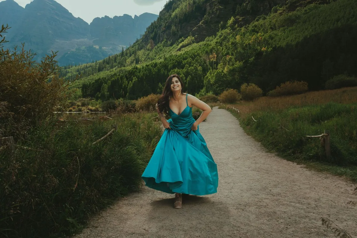 Woman in a teal evening gown and hiking boots on a mountain trail