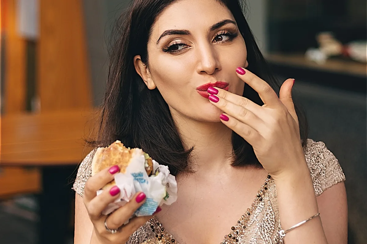 Woman in a gold lace evening dress eating a burger