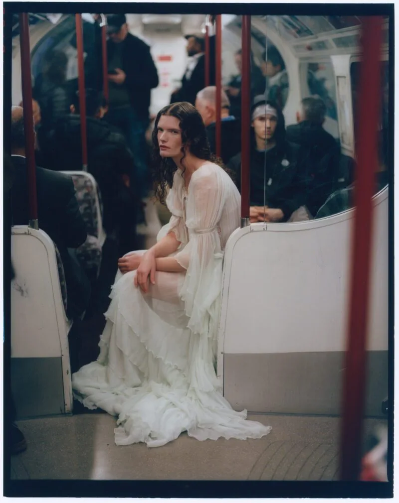 Woman in a white sheer gown sitting on a subway seat