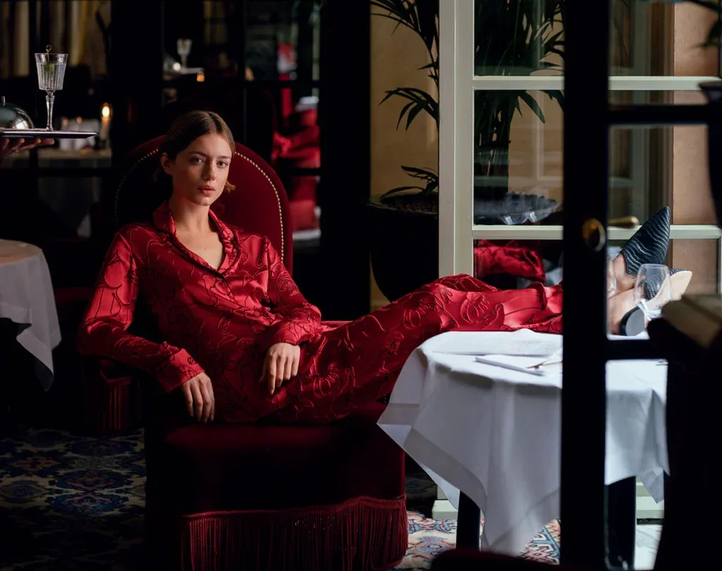 Woman in red satin pajamas reclining at a fancy restaurant table