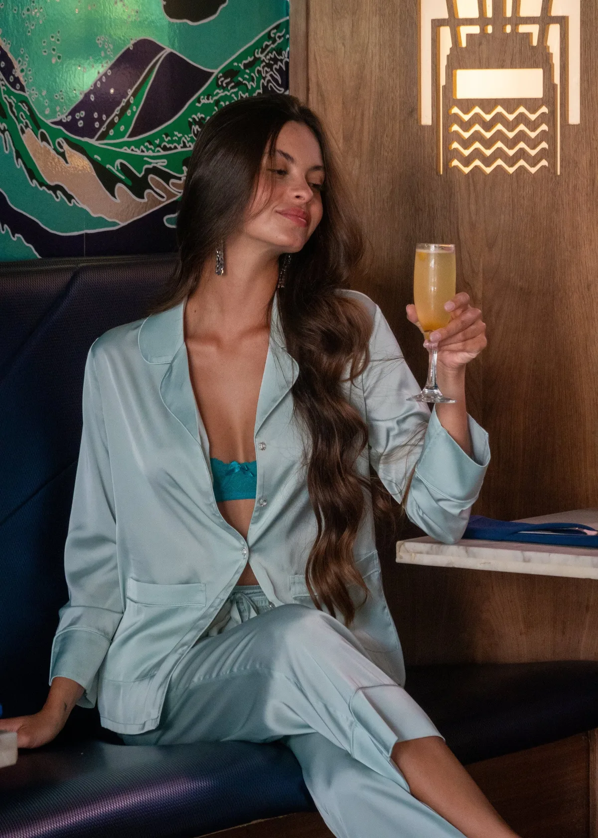 Woman in mint silk pajamas holding a cocktail at a bar