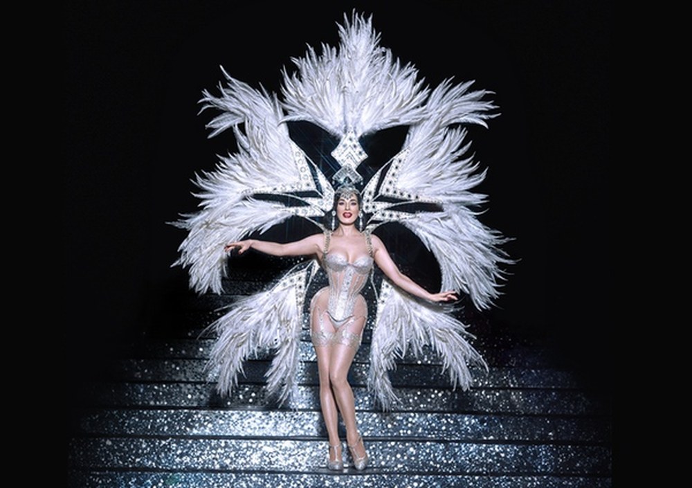 Showgirl with large white feather backpiece on stairs