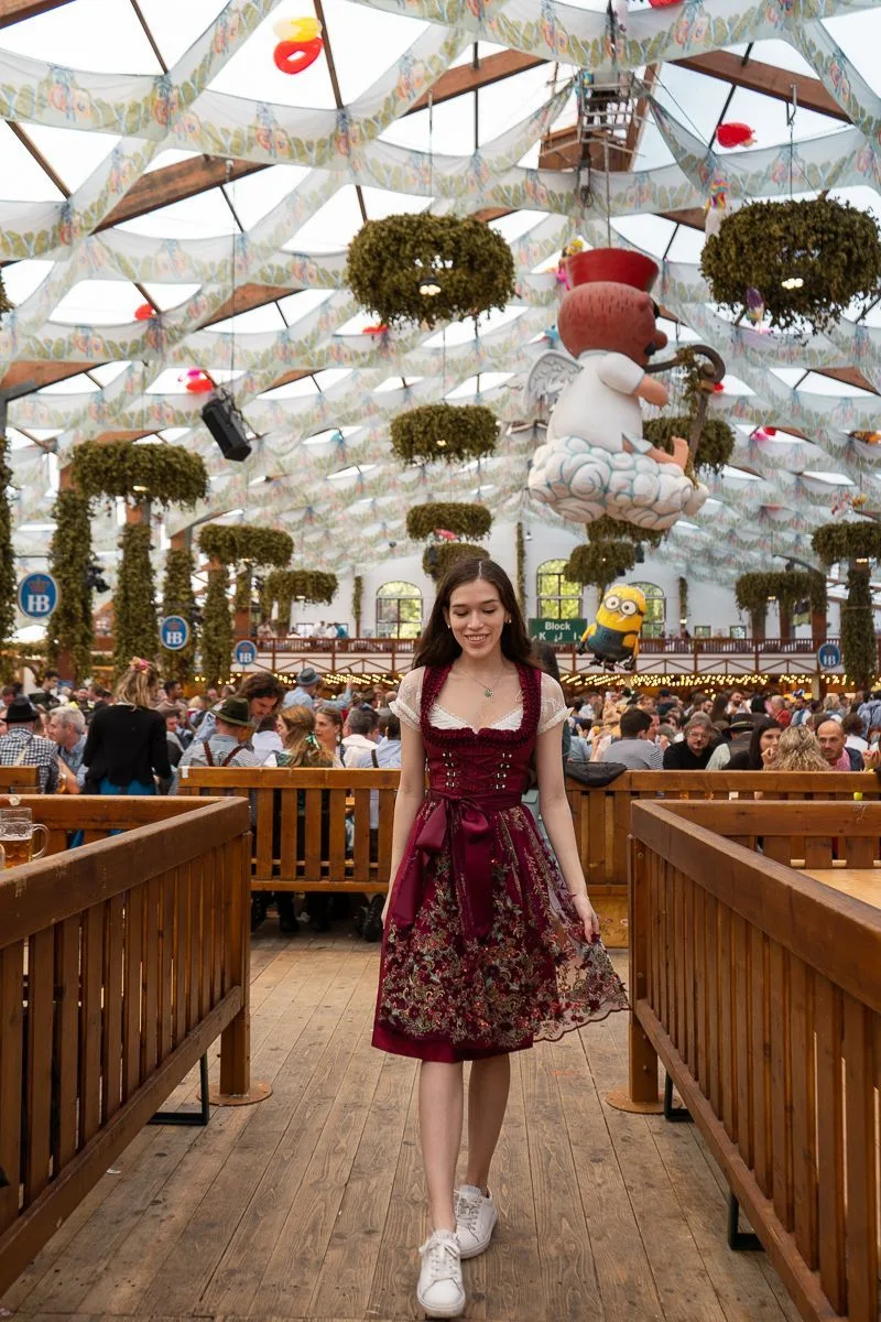 Woman in a dark red floral dirndl walking inside a decorated Oktoberfest beer tent