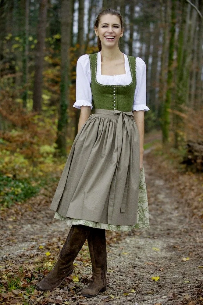 Woman in an olive green dirndl with brown boots on a forest path