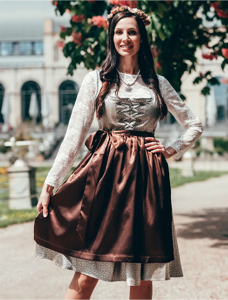 Woman in a chocolate brown dirndl with a lace blouse and flower crown in a park