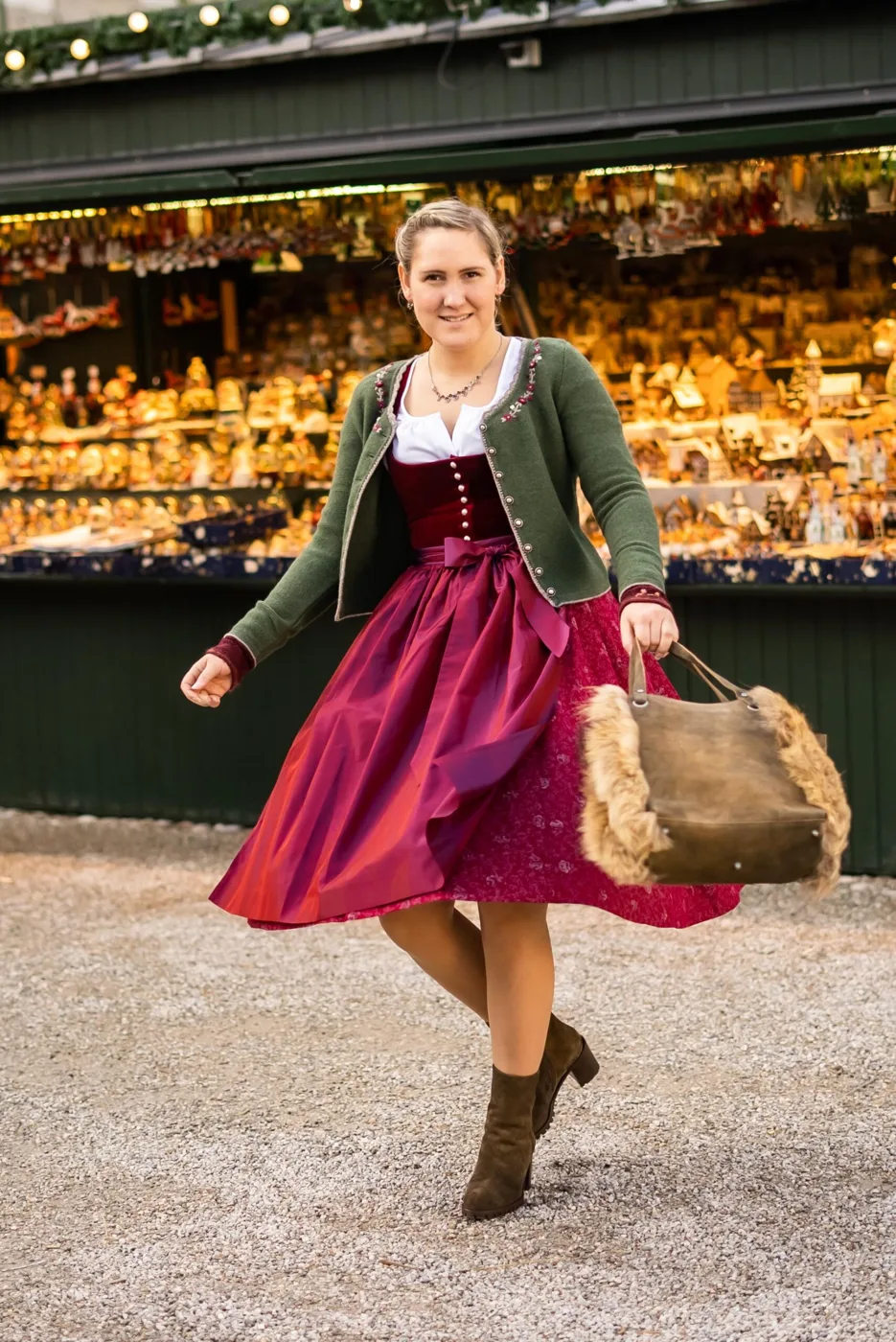 Woman in a magenta dirndl with a green cardigan and boots at a market stall