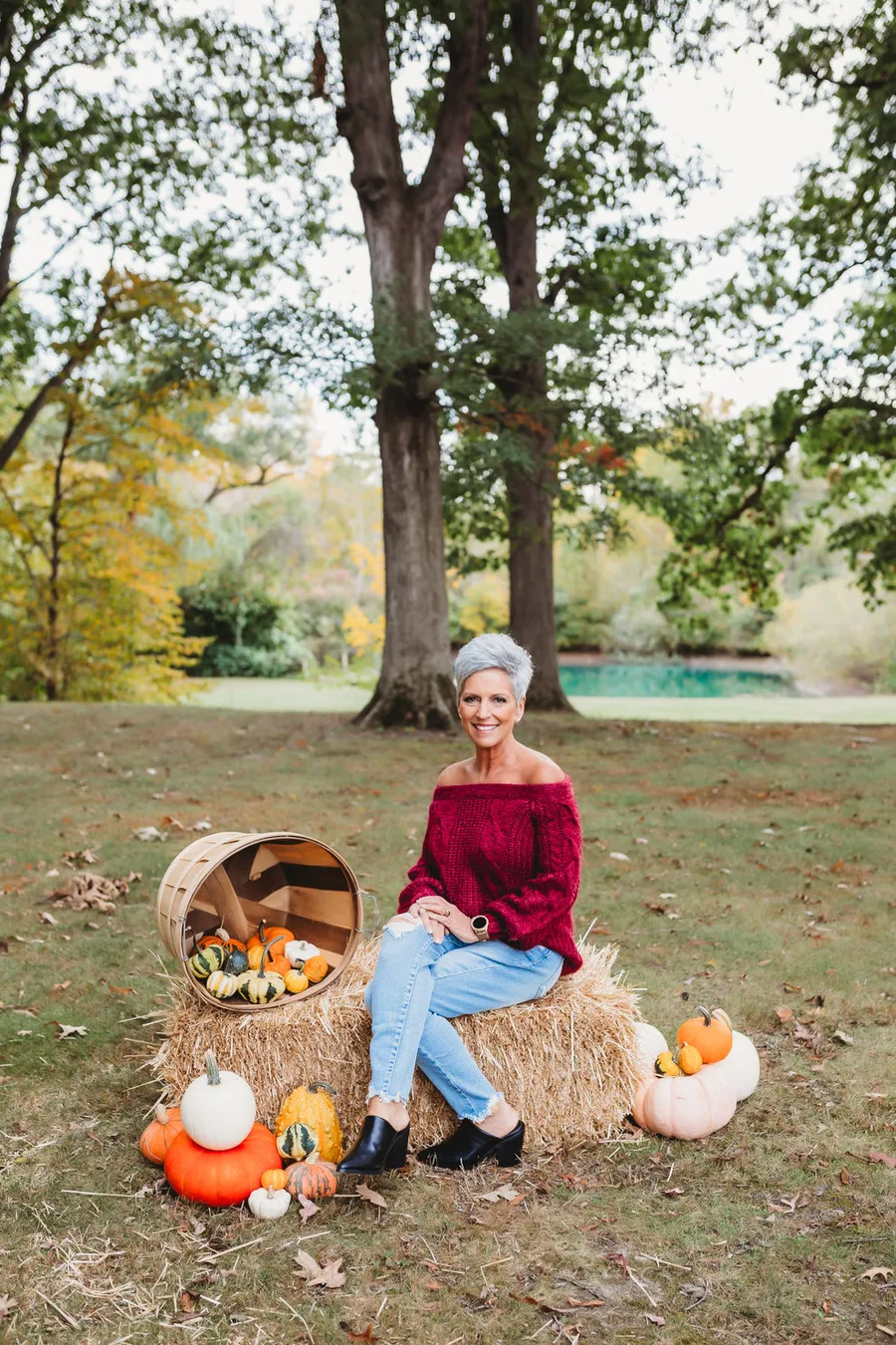 Pumpkin patch outfit for women over 50: red top with jeans sitting on hay bales